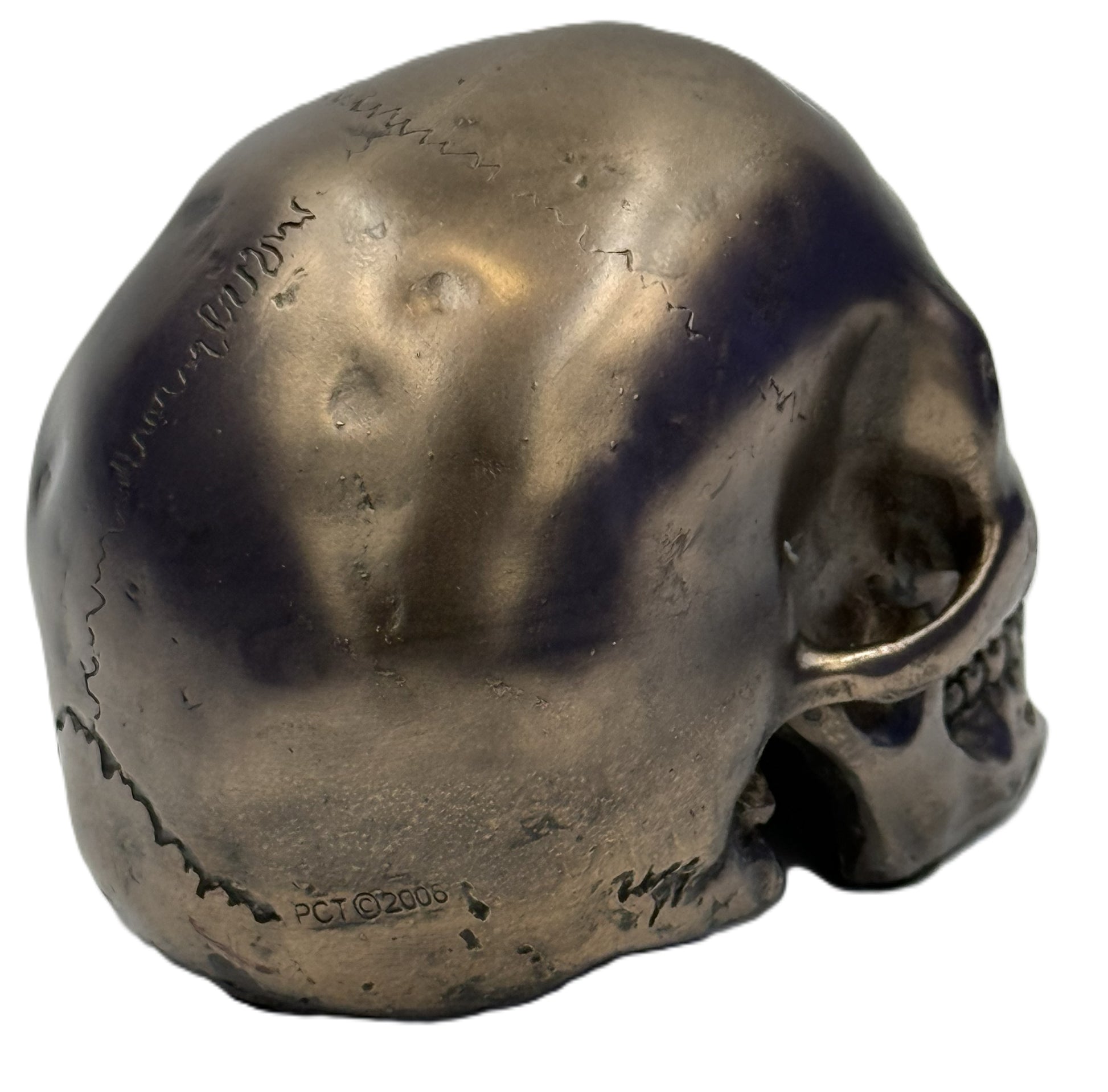 Side view of small bronze skull figurine highlighting sculpted bone structure and weathered finish
