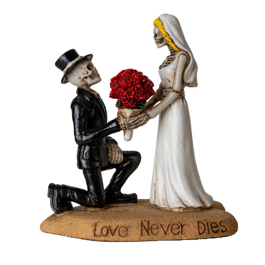 Front view of skeleton bride and groom statue with red rose bouquet and love never dies engraving
