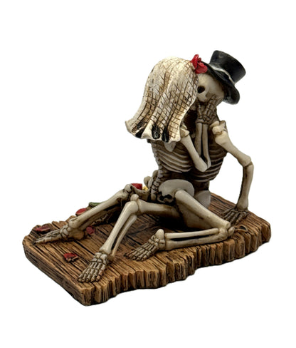 Side view of gothic skeleton couple decor with intertwined pose and scattered red rose petals
