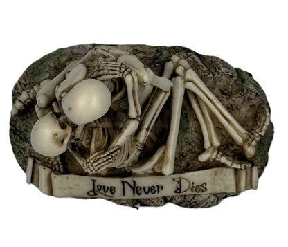 Top view of skeleton couple statue showing close embrace and Love Never Dies engraving on base

