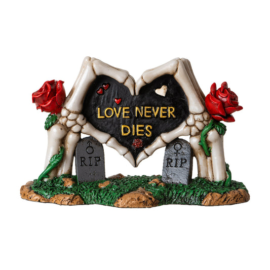 Front view of skeleton hands forming heart statue with love never dies text and red roses
