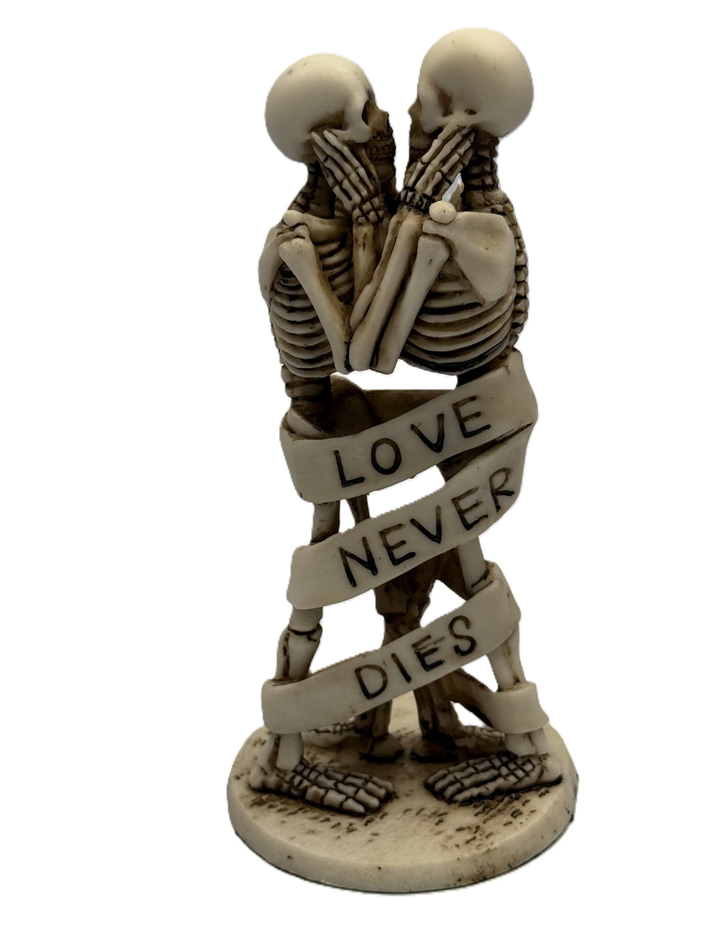 Front view of gothic skeleton couple statue standing and embracing with “Love Never Dies” ribbon wrapped around bodies
