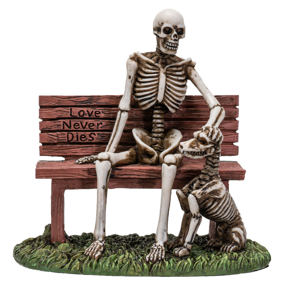Front view of skeleton sitting on bench with skeletal dog and “Love Never Dies” engraving
