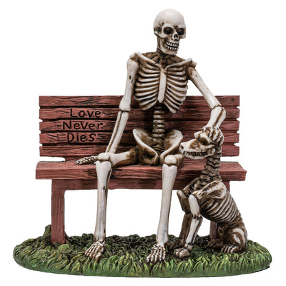 Front view of skeleton sitting on bench with skeletal dog and “Love Never Dies” engraving

