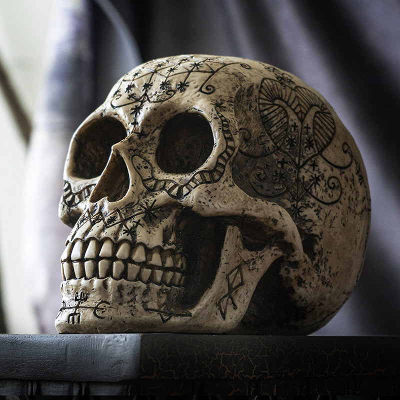 Left side view of voodoo skull statue with etched occult patterns and aged finish
