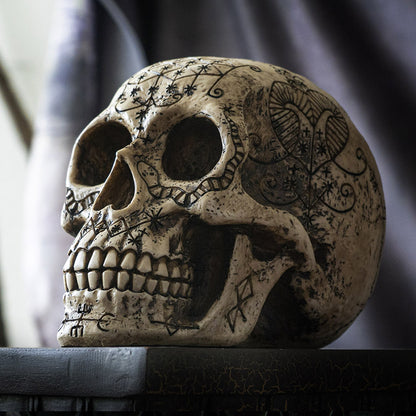 Left side view of voodoo skull statue with etched occult patterns and aged finish
